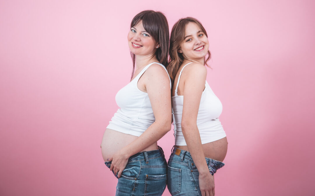 Dos mujeres embarazadas sonríen de espaldas en fondo rosa, representando el bienestar materno y la atención ginecológica moderna en Quito.