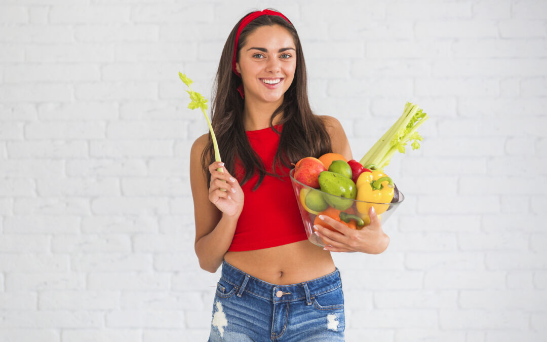 Mujer sonriente sosteniendo un cuenco con frutas y vegetales saludables, símbolo de una dieta equilibrada que ayuda a prevenir infecciones vaginales y mantener la flora vaginal sana