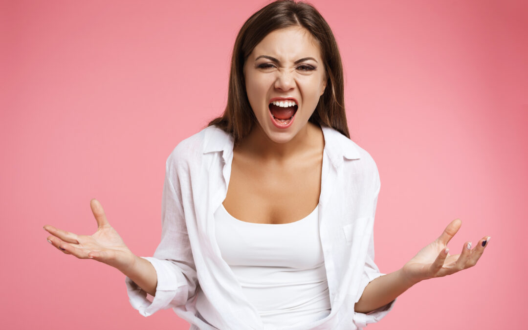 Mujer joven expresando frustración y cambios emocionales relacionados con el síndrome premenstrual; fondo rosado, representa el impacto hormonal y emocional del ciclo femenino.